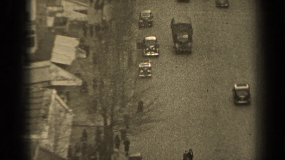 1947 Paris street seen from above, with small automobiles traveling along a paved road beside bare trees and building edges.