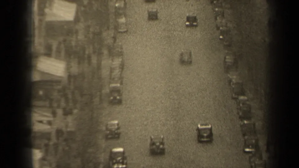 Elevated 1947 Paris traffic view showing cars on a broad roadway with parked vehicles and multi-story buildings at the edge.