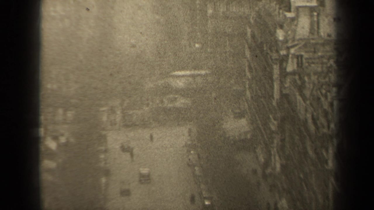 1947 Paris street view from above, with small cars and pedestrians below tall European-style buildings, partly obscured by dark frame edges.
