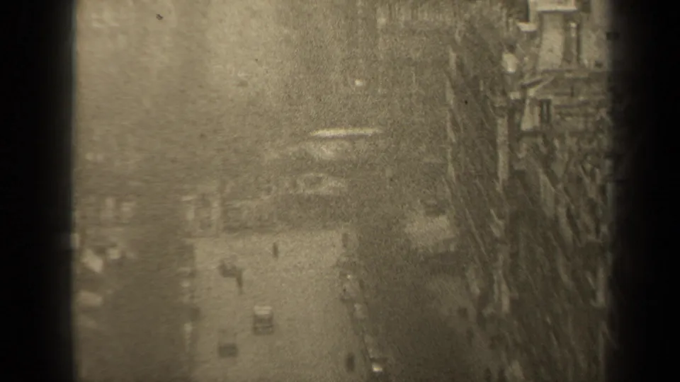 1947 Paris street view from above, with small cars and pedestrians below tall European-style buildings, partly obscured by dark frame edges.