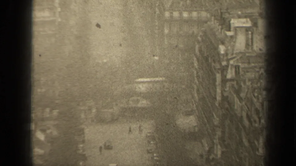 High-angle 1947 Paris street scene with distant pedestrians, cars, bare trees, and rows of buildings seen through soft, grainy 8mm footage.