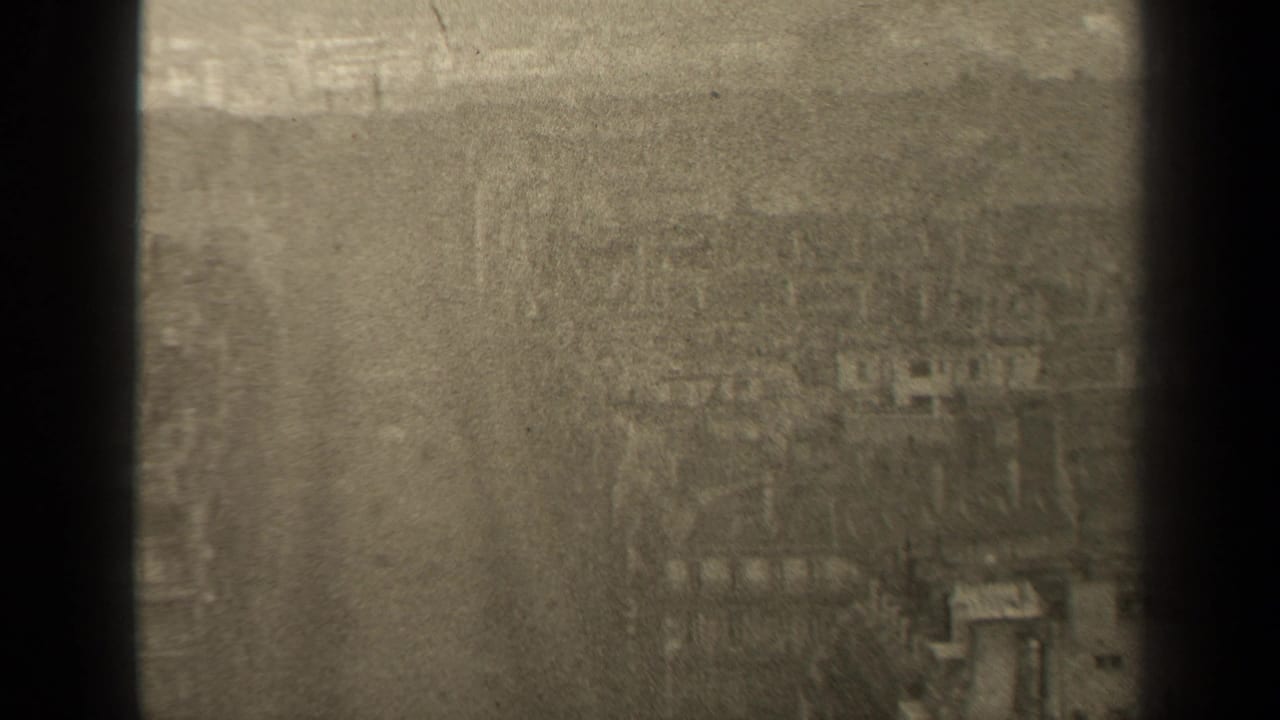 High-angle 1947 Paris street view with a broad roadway, bare trees, sidewalks, and soft building forms seen through grainy 8mm footage.