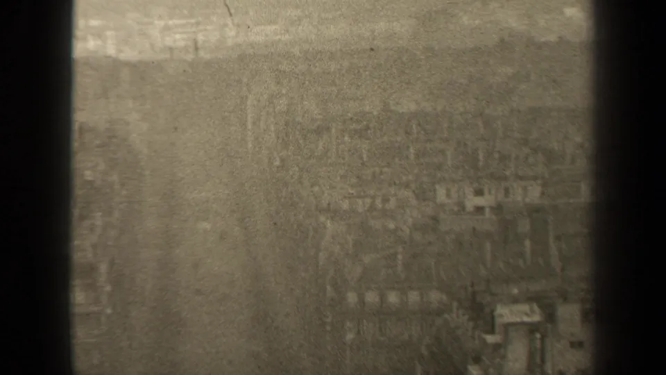 High-angle 1947 Paris street view with a broad roadway, bare trees, sidewalks, and soft building forms seen through grainy 8mm footage.