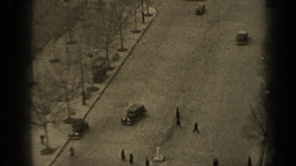 High-angle 1947 Paris view with a car on the road, pedestrians crossing, bare street trees, sidewalks, and dark film-edge borders.