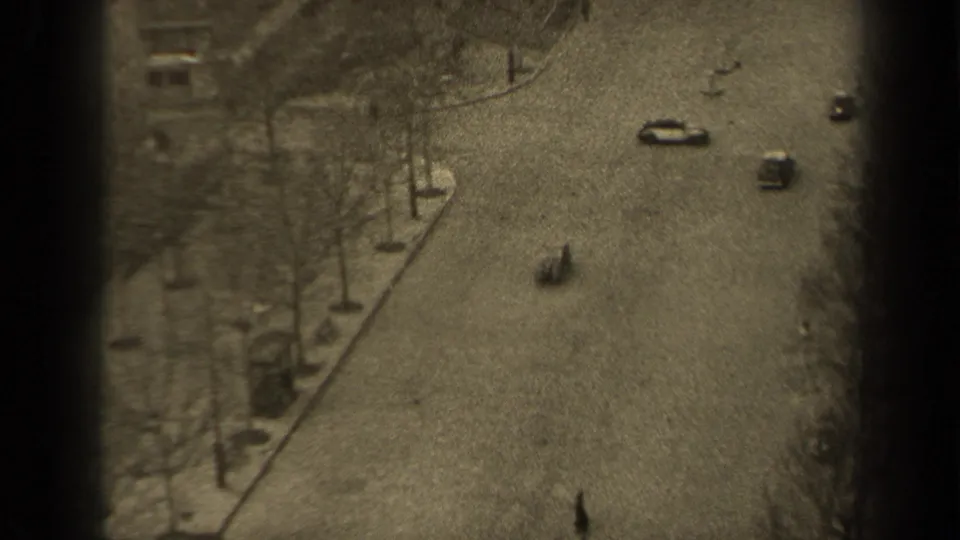 Grainy 1947 Paris street view from above, with several cars, scattered pedestrians, bare trees, sidewalks, and soft exposure shifts.