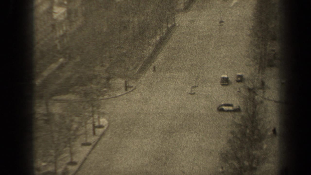 Elevated view of a broad road with cars, bare trees, and pedestrians near the sidewalk.