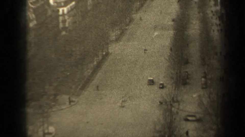 1947 Paris 8mm frame looking down on a quiet street with a few cars, bare trees, sidewalks, and a building edge.