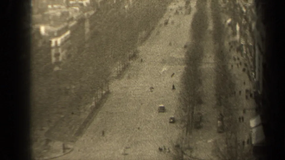 Elevated 1947 Paris street frame with cars, distant pedestrians, bare trees, sidewalks, and dark 8mm frame borders.
