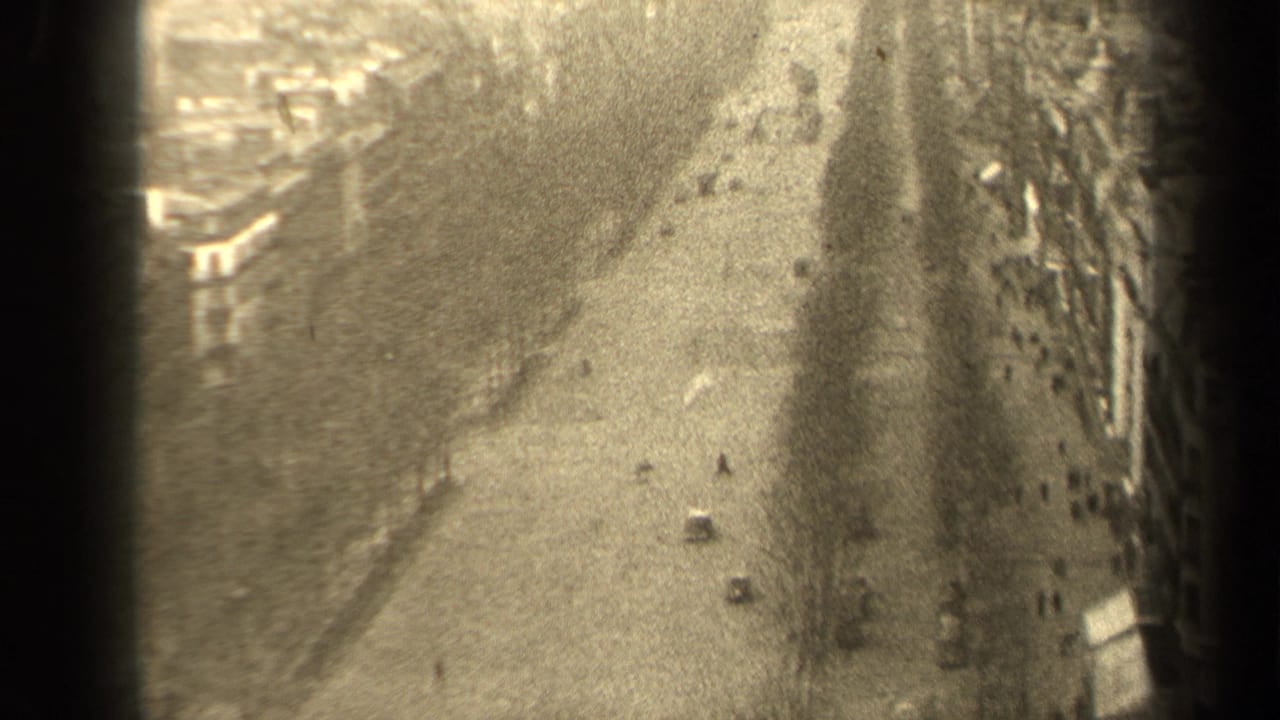 High-angle view of a broad city street with cars, pedestrians, buildings, and dark film edges.