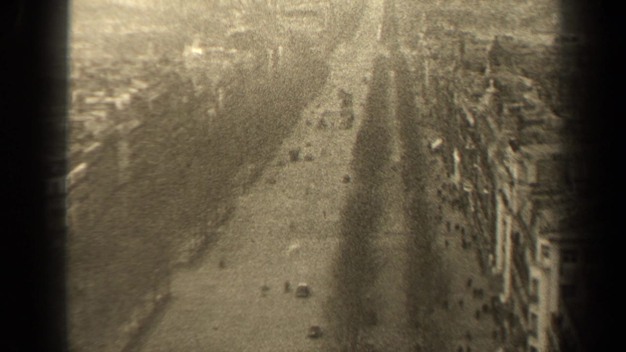 Elevated street view with automobiles, pedestrians, building frontage, and a dark vertical film border.