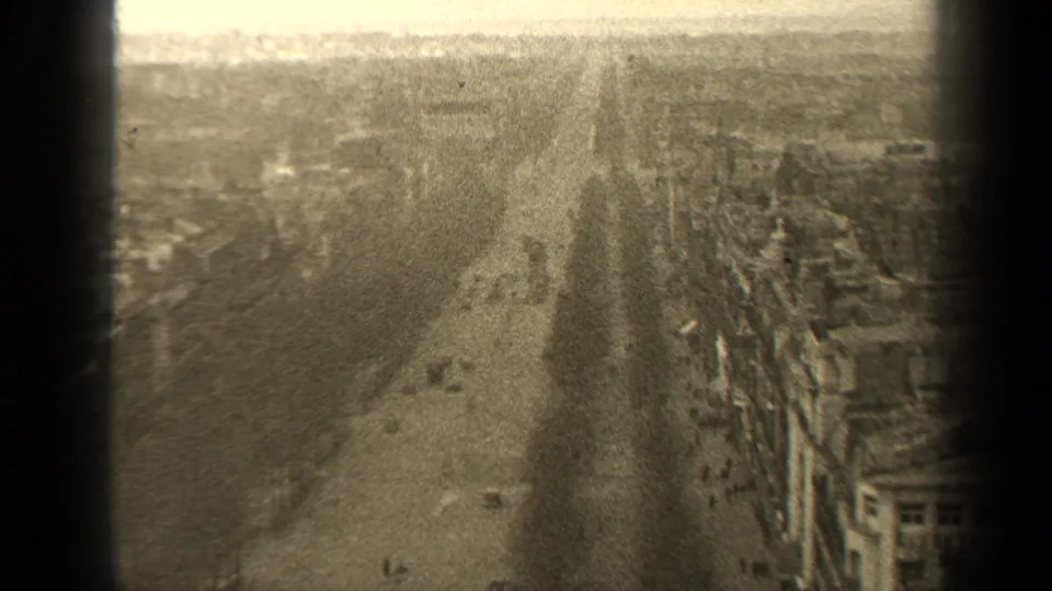 A soft 1947 Paris street frame shows light automobile traffic, distant pedestrians, building frontage, and pronounced 8mm grain.