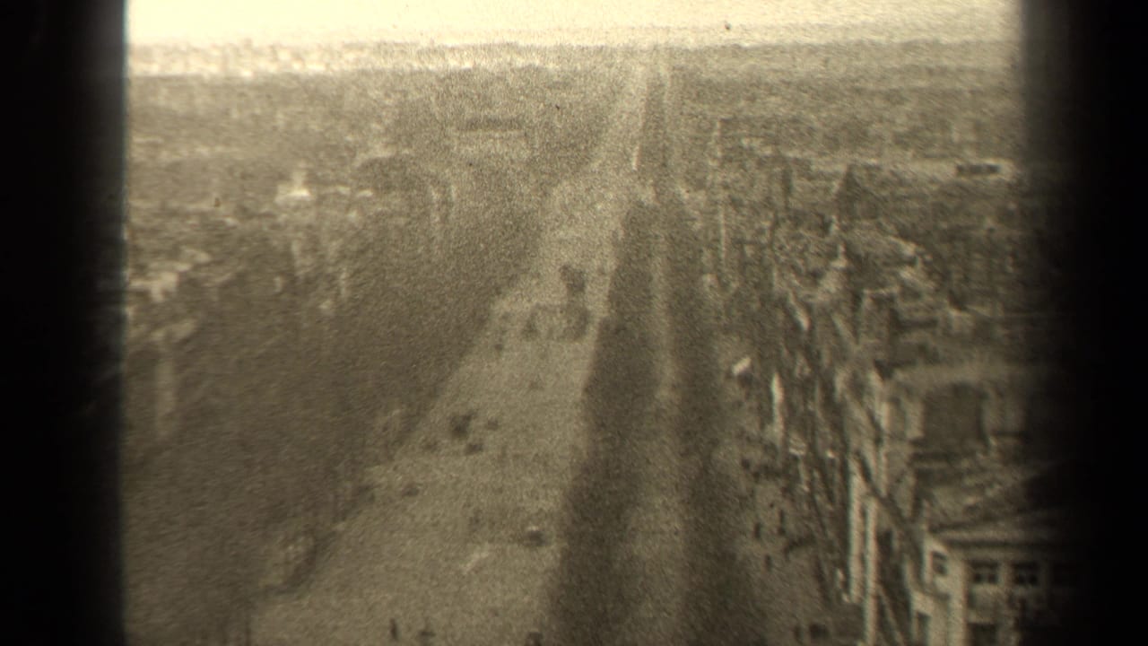 1947 Paris home-movie view looking down a broad street from above, with bare trees, buildings, and soft sepia exposure.
