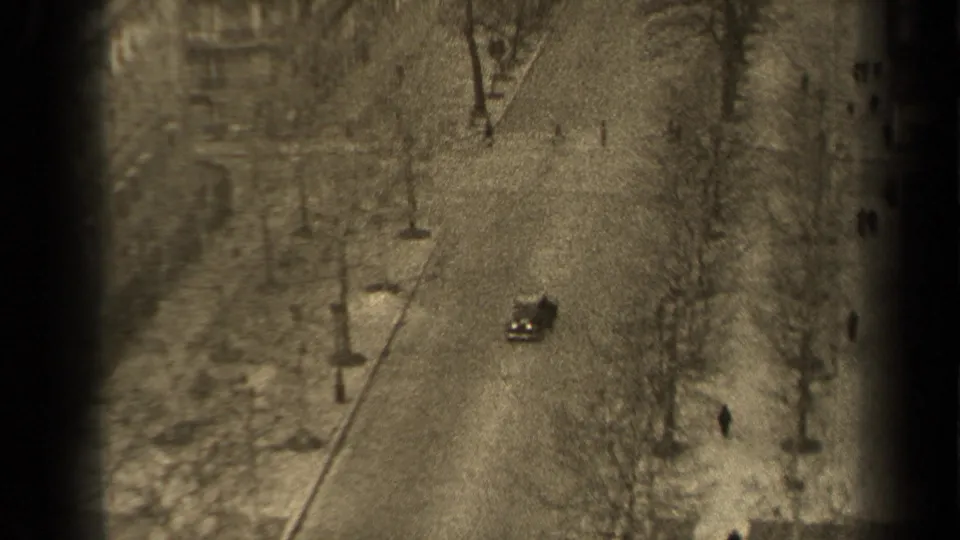1947 Paris street seen from an upper window, showing a car on the road, pedestrians nearby, bare trees, and streetlamps.