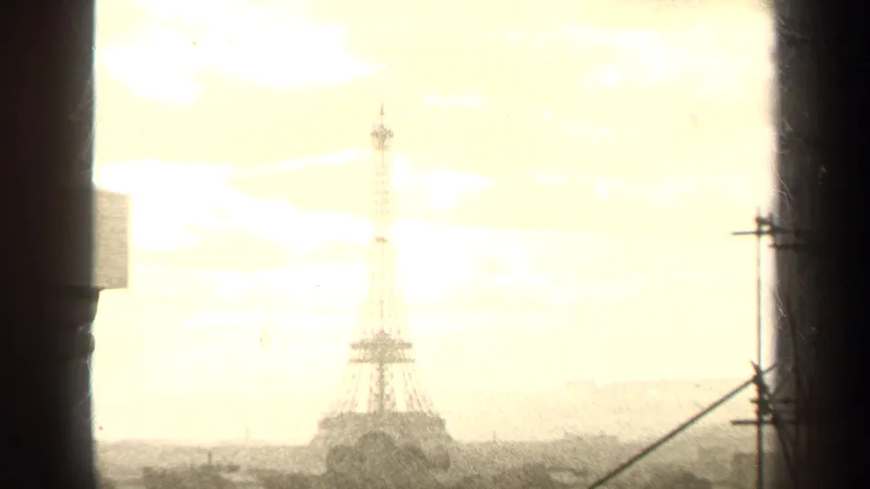 Distant Eiffel Tower in Paris framed through a window or structural edge, with bright sky and visible 8mm film grain.
