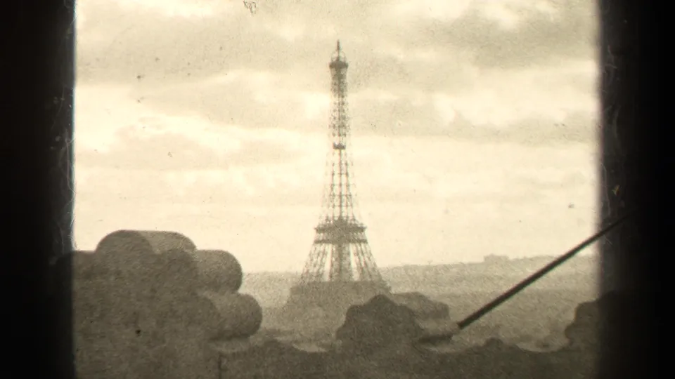 1947 Paris home-movie frame showing the Eiffel Tower at a distance through a dark window frame under a cloudy sky.