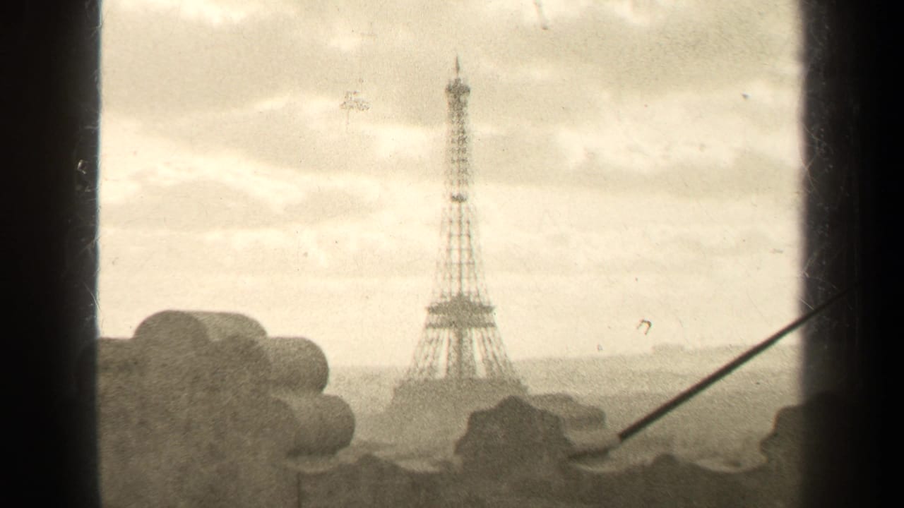 1947 Paris home-movie frame showing the Eiffel Tower from an elevated window or balcony with cloudy sky and hazy distance.