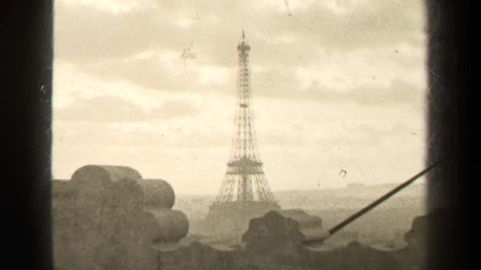 1947 Paris home-movie frame showing the Eiffel Tower from an elevated window or balcony with cloudy sky and hazy distance.