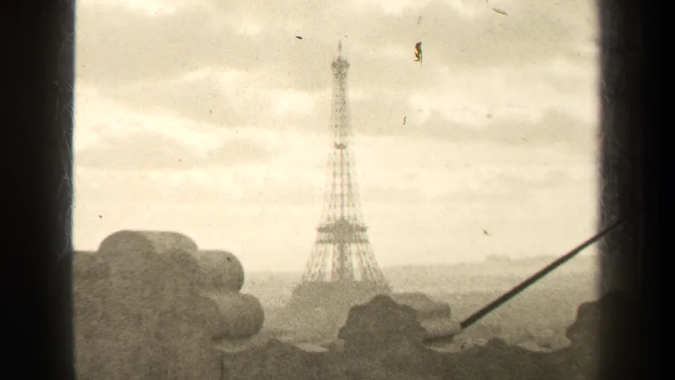 1947 Paris frame showing the Eiffel Tower through a high opening, with pale cloud cover, visible film wear, and foreground masonry.