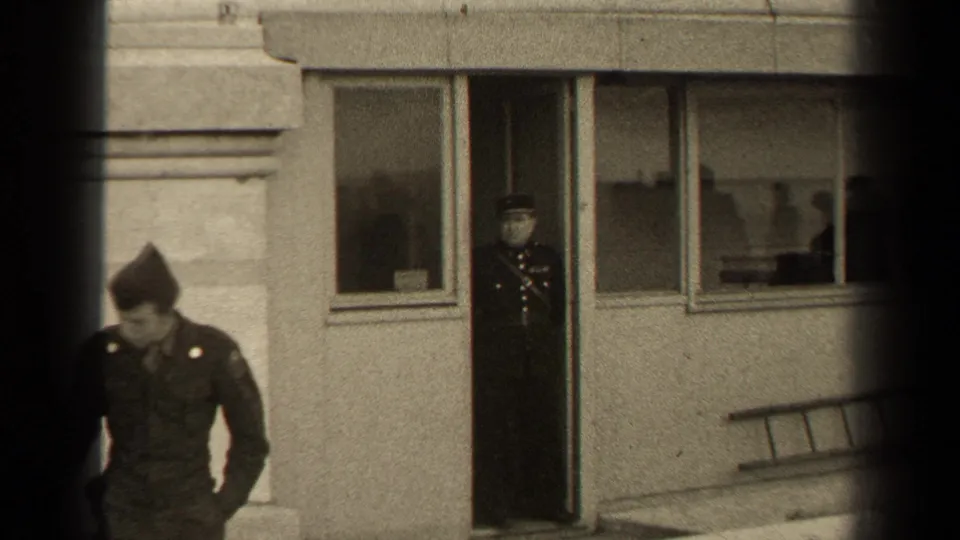 Paris 1947 frame with a passerby moving across the foreground while a uniformed man remains in a building doorway.