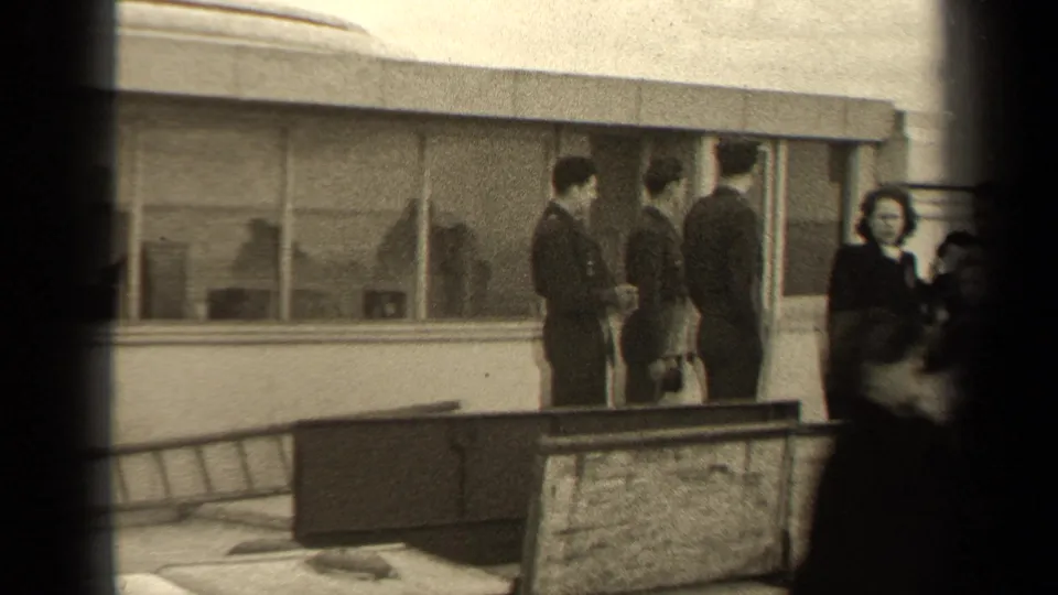 Several civilians gather or pass outside the Paris building, with windows, a ladder, and a low barrier visible in the frame.