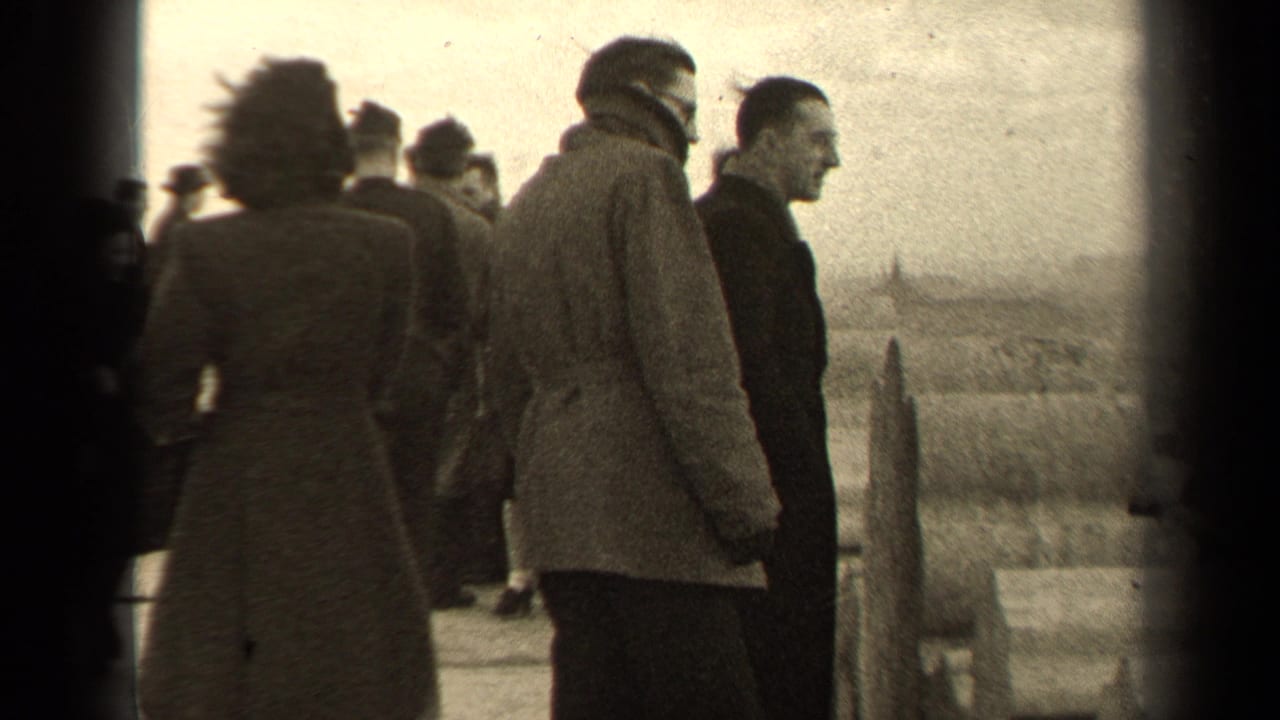 In 1947 Paris home-movie footage, bundled adults stand and talk on a windswept overlook with open landscape beyond.