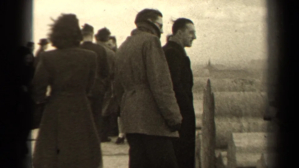 In 1947 Paris home-movie footage, bundled adults stand and talk on a windswept overlook with open landscape beyond.
