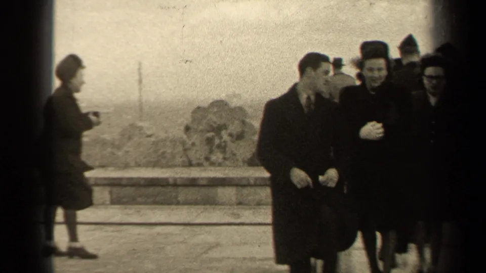 Bundled adults smile near a windswept Paris overlook, with open sky and distant ground visible behind them.