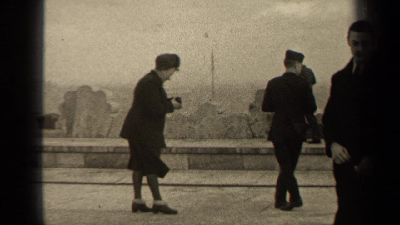 A woman with a camera leans forward as uniformed and formally dressed people stand nearby.
