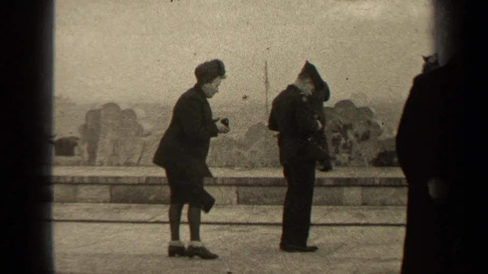 1947 Paris home-movie frame showing a woman with a camera facing a uniformed man near a stone promenade.