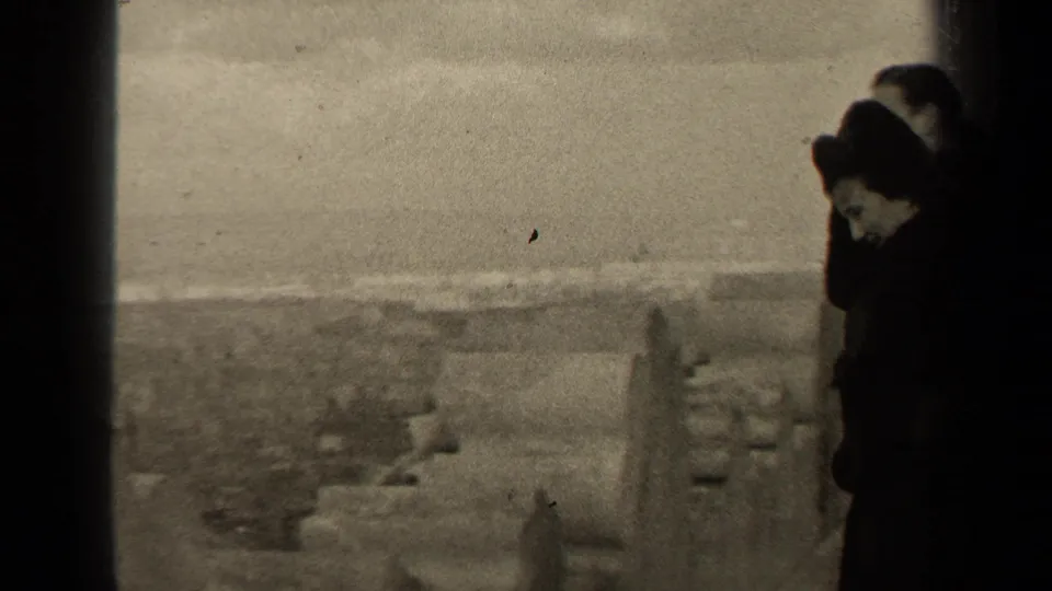In 1947 Paris home-movie footage, two figures in dark clothing stand near a high ledge overlooking the city.