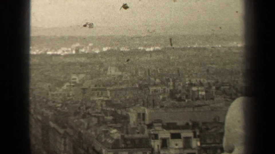 1947 8mm home-movie view over Paris rooftops, seen through dark vertical frame edges with a hazy horizon.