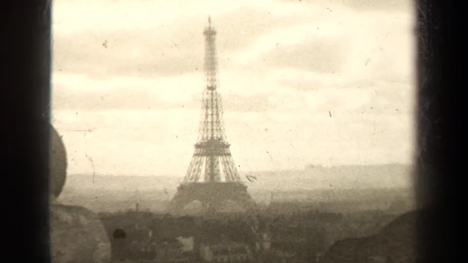 1947 8mm view of the Eiffel Tower in Paris, framed by dark edges with rooftops and cloudy sky visible.