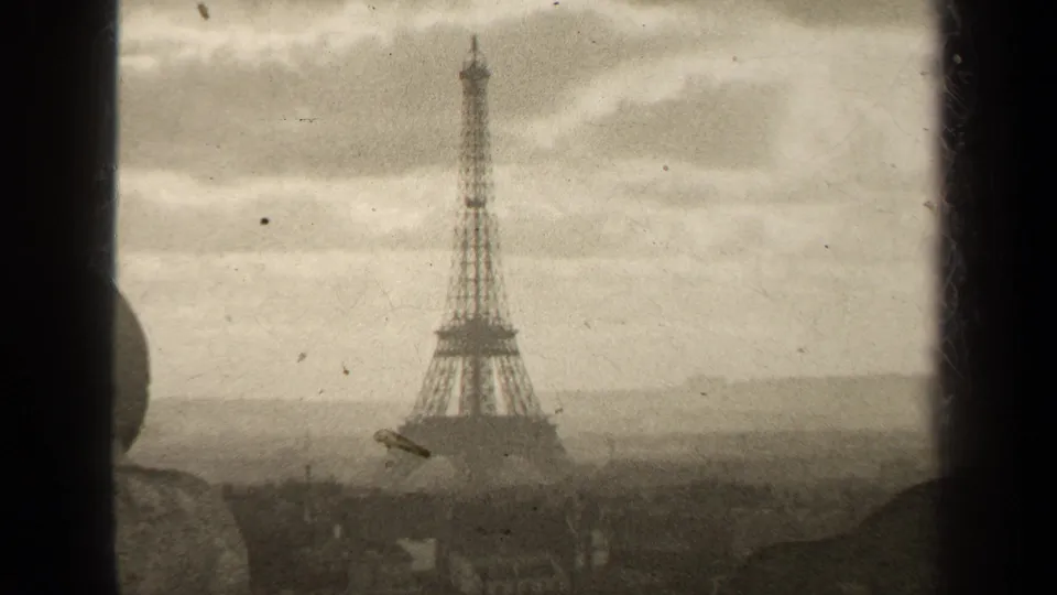 Centered 1947 Paris view of the Eiffel Tower, with haze near the skyline, cloudy sky, and visible 8mm film dust.