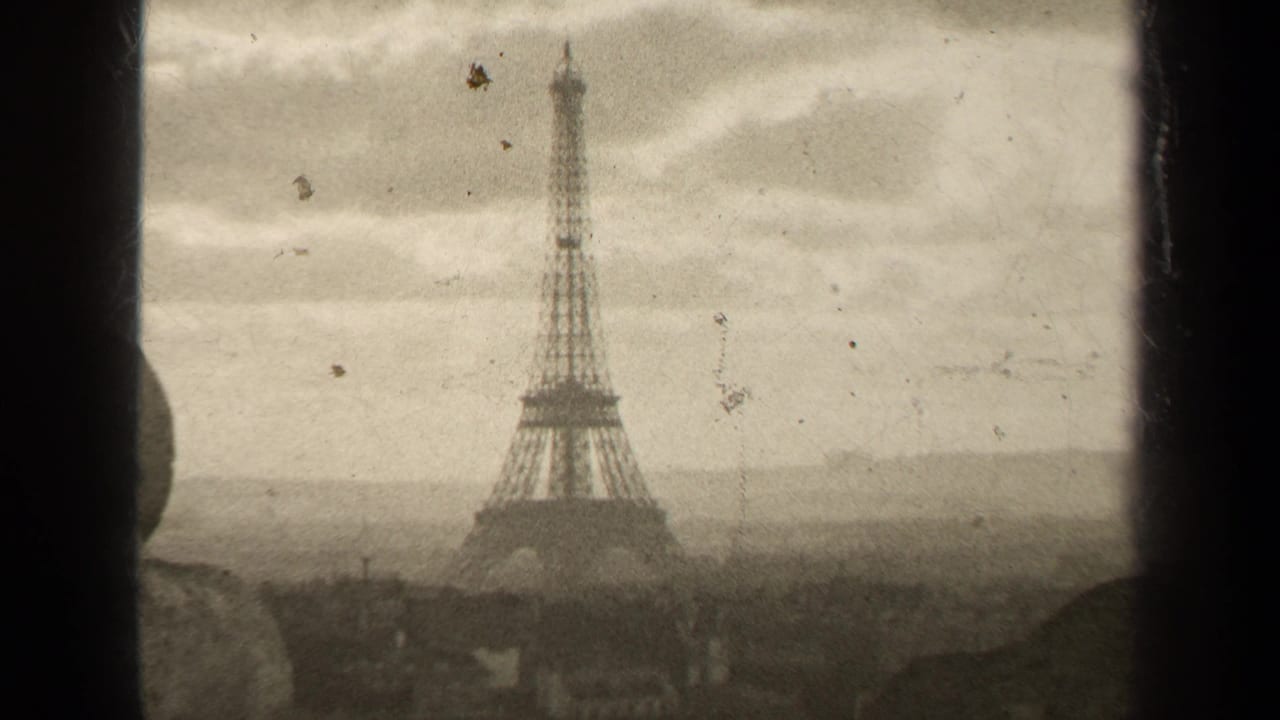 1947 8mm view of the Eiffel Tower in Paris beneath an overcast sky, with hazy rooftops and visible film grain.