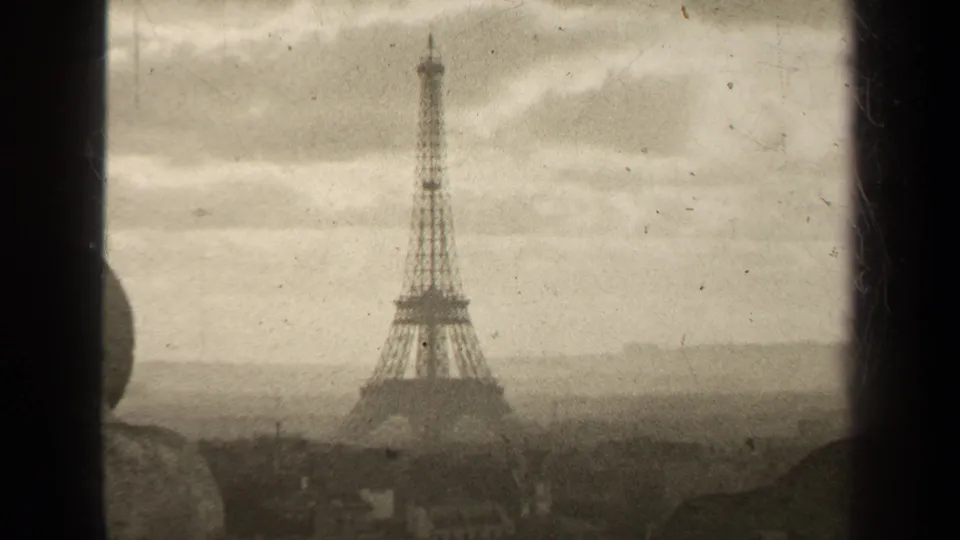 1947 Paris home-movie frame of the Eiffel Tower under a dull sky, bordered by dark 8mm film edges and visible dust.