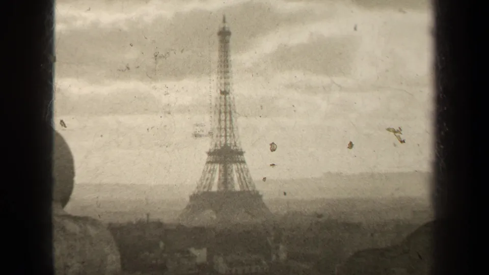 1947 Paris home-movie frame showing the Eiffel Tower through a window with hazy rooftops and visible 8mm film wear.