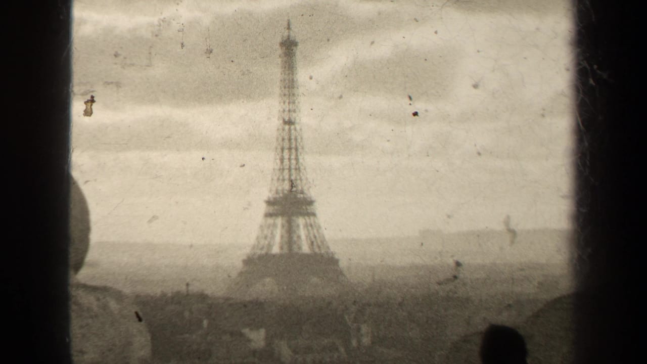 Eiffel Tower seen through a soft, grainy film frame under a cloudy sky.
