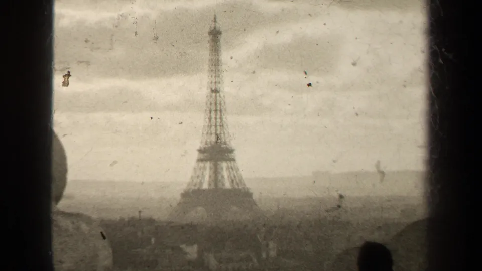 1947 Paris home-movie frame showing the Eiffel Tower above rooftops in soft sepia-toned 8mm footage.