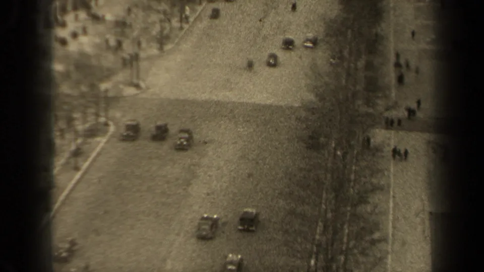 1947 Paris street traffic seen from above, with cars crossing the frame and pedestrians along a tree-lined sidewalk.