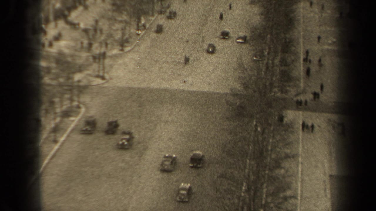 1947 Paris home-movie view from above showing cars on a broad boulevard and pedestrians along large sidewalks.
