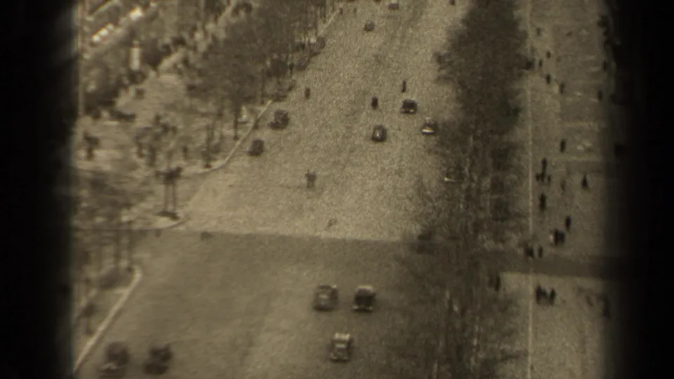High-angle 1947 Paris street scene with scattered automobiles, pedestrians and tree-lined sidewalks in soft 8mm footage.
