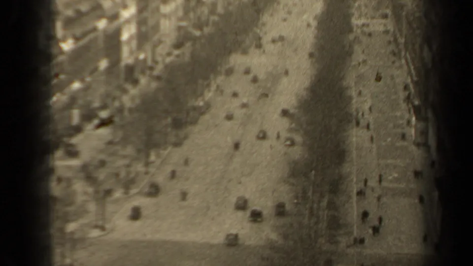 Soft 8mm frame of a 1947 Paris boulevard, with scattered cars, pedestrians and trees along the roadway.