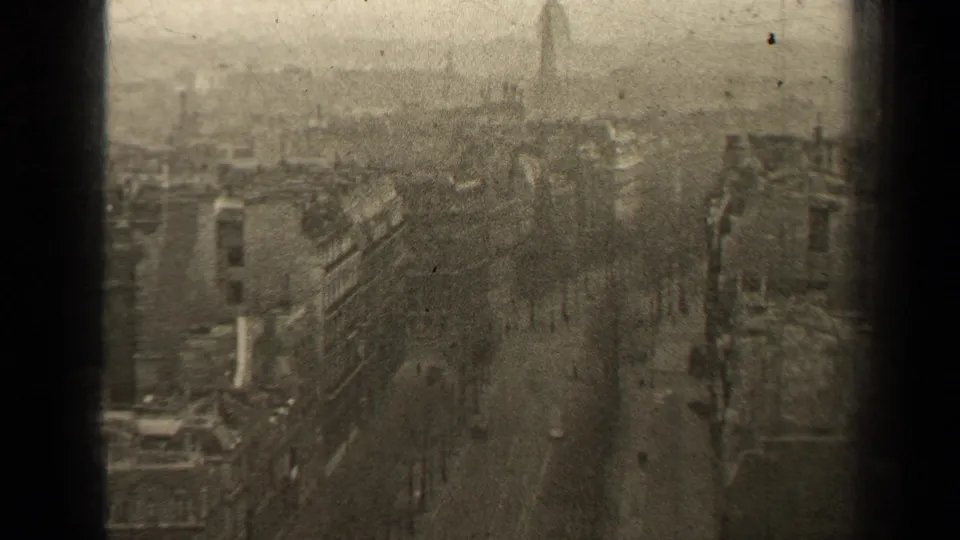 Elevated 1947 Paris view across rooftops, a tree-lined street, distant pedestrians, and a hazy skyline in worn 8mm black-and-white footage.