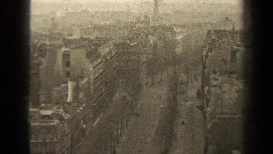 1947 Paris street scene from above, with rooftops, bare boulevard trees, small cars, and pedestrians softened by grain and surface wear.