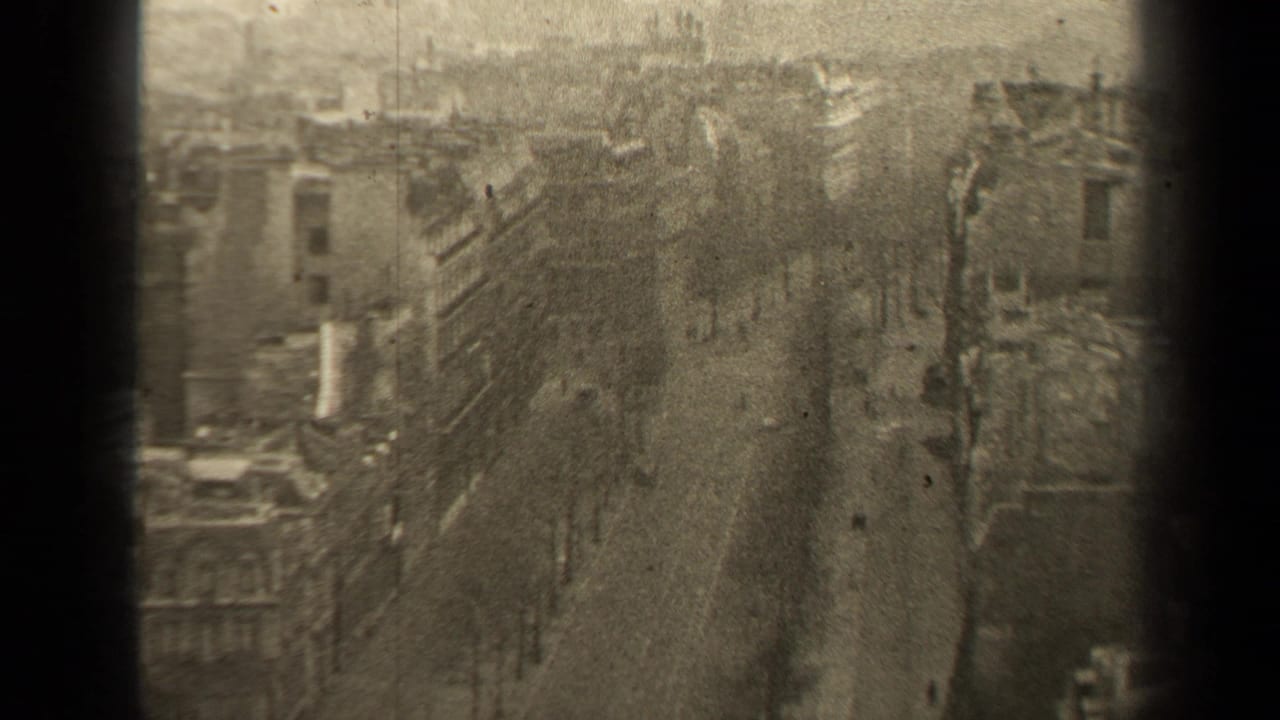 High-angle view of a broad Paris boulevard with buildings, trees, pedestrians and small cars.