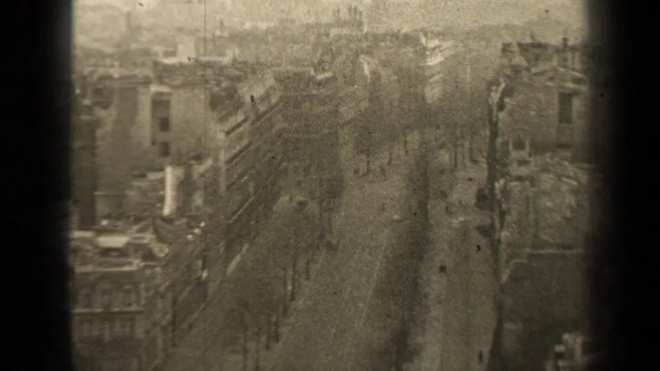 1947 Paris street scene from above, showing a broad boulevard lined with buildings, bare trees, pedestrians and sparse vintage car traffic.