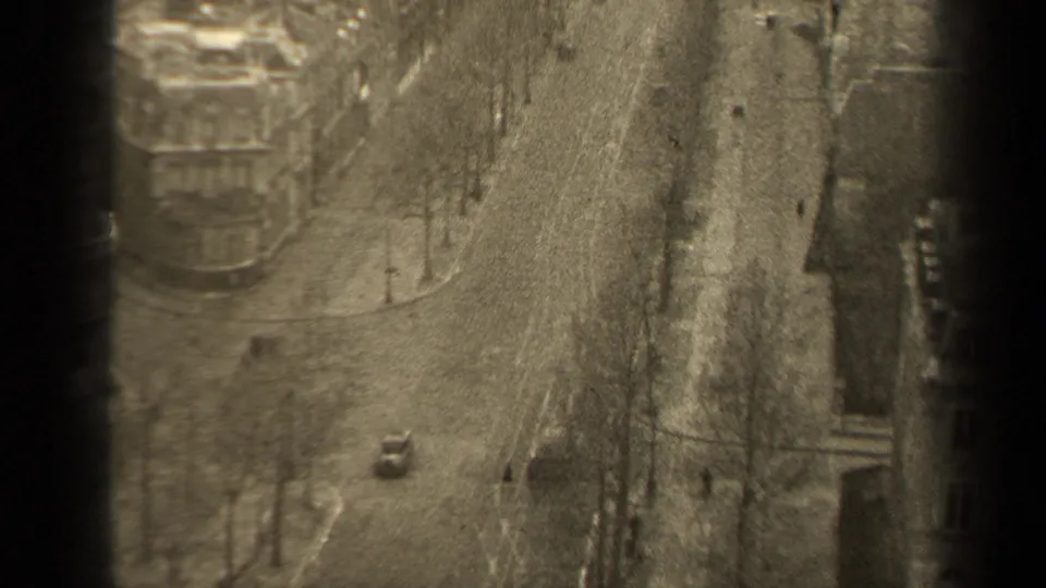 High-angle 1947 Paris street view with bare winter trees, scattered pedestrians, sidewalks, and a small car below.