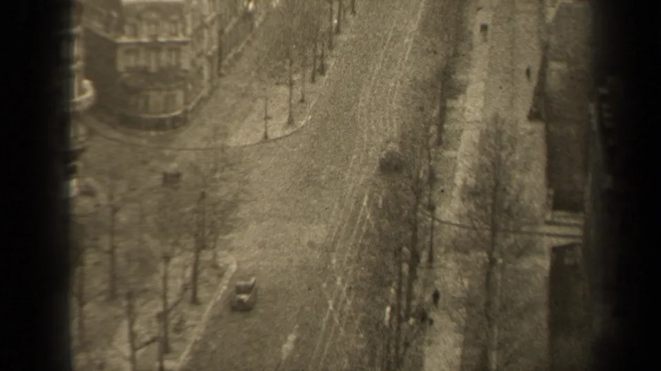 Soft-focus 1947 Paris street frame with winter trees, a small car, pedestrians, sidewalks, and surrounding building fronts.