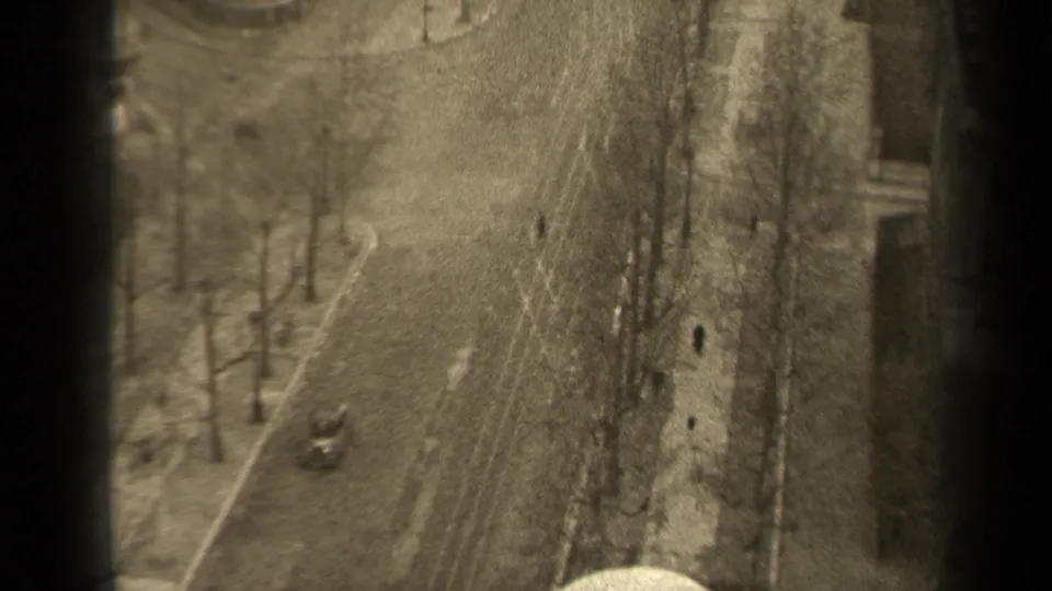 Elevated 1947 Paris street view with a lightly trafficked road, bare trees, old building facades, and tiny pedestrian figures.