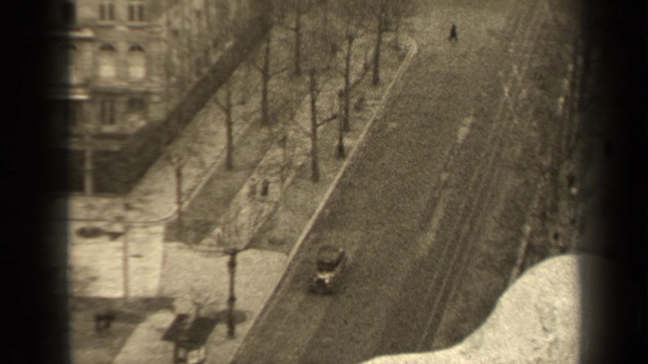 High-angle view of a tree-lined Paris street with sidewalks, buildings, pedestrians, and a small car.